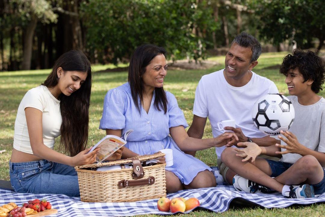A family with a teenage daughter and son holding a soccer ball having a picnic