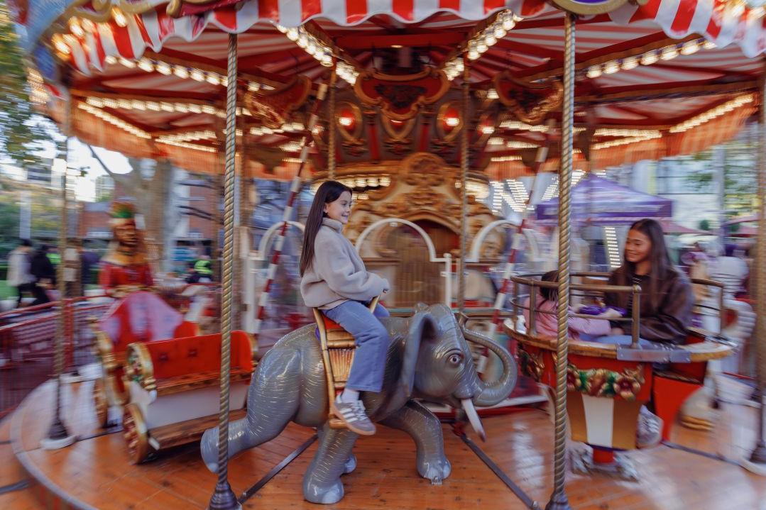 A child joyfully rides an elephant figure on a moving carousel. Warm lighting, vintage decor, and blurred motion create a festive, nostalgic ambiance.