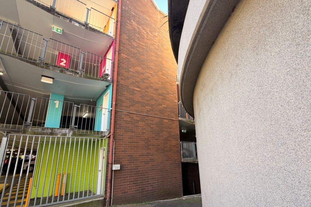A grey curved wall, with a brick wall and a lim green wall in the background
