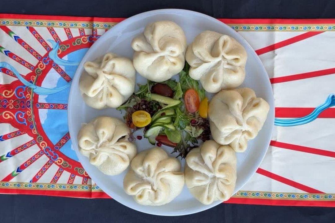 Plate of steamed buuz dumplings arranged in a circle around a small mixed salad of lettuce, cucumber and cherry tomatoes.