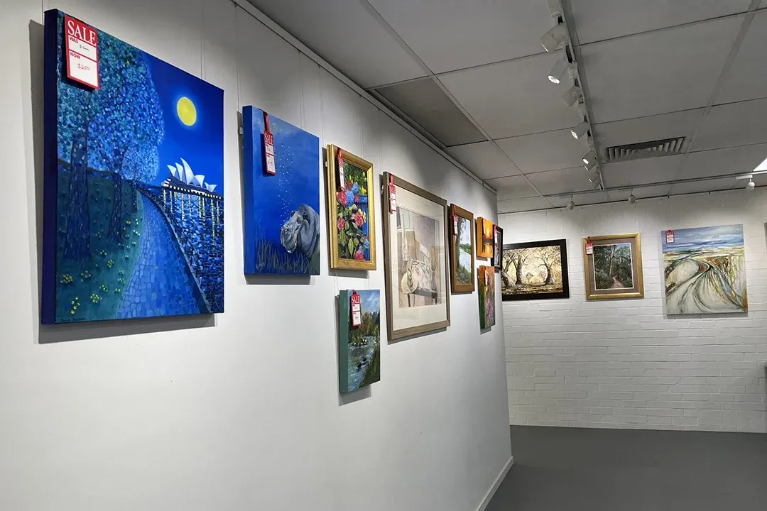 A gallery interior featuring various paintings on the walls, accompanied by an informational sign.