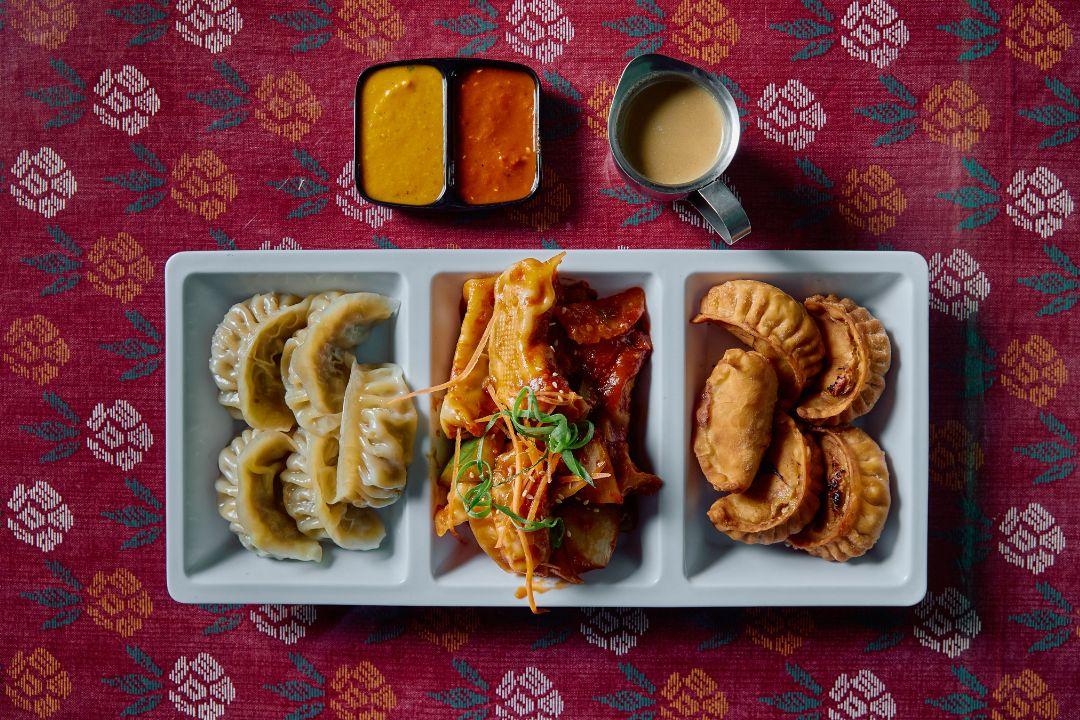 A divided serving platter featuring three varieties of dumplings on a patterned red tablecloth.