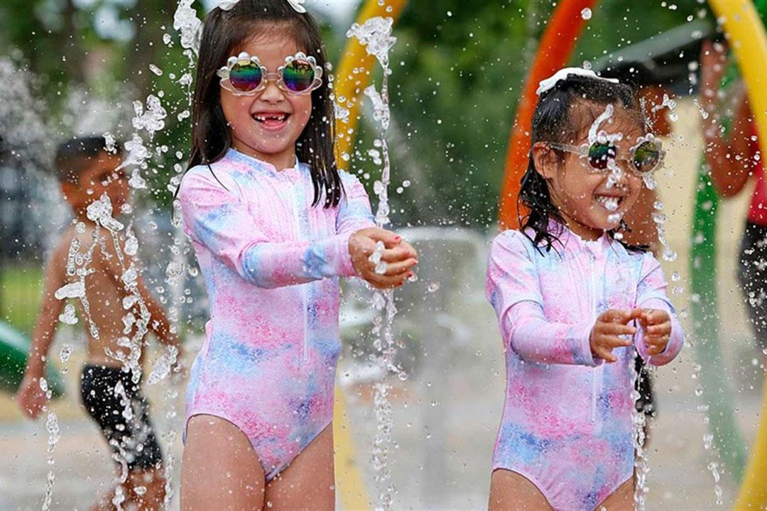 Two young girls in colourful swimsuits joyfully playing together at a vibrant water park.