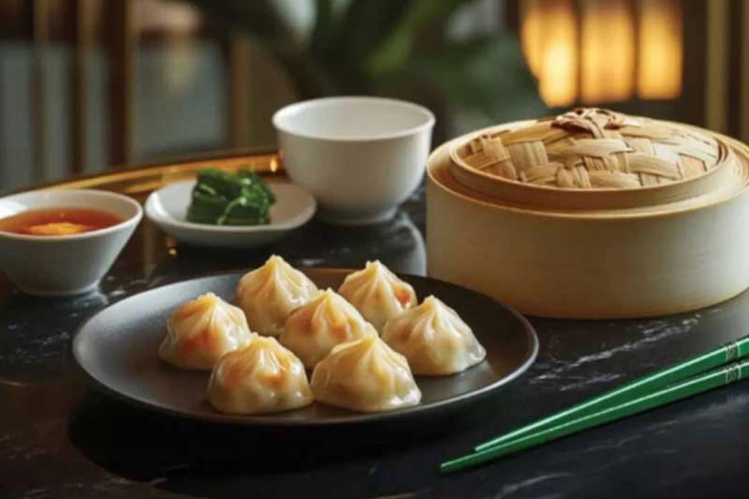 Six xiao long bao soup dumplings served on a black plate beside a bamboo steamer basket.