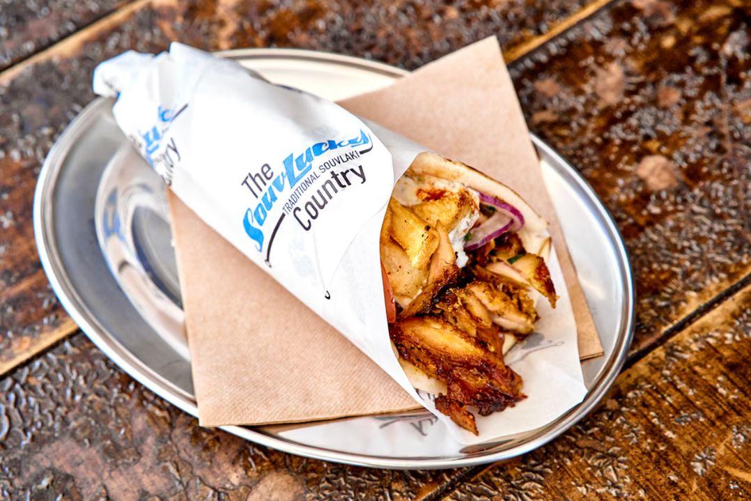 Wrapped souvlaki filled with grilled chicken, tomato, onion and fresh toppings, served on a metal tray lined with a paper napkin.
