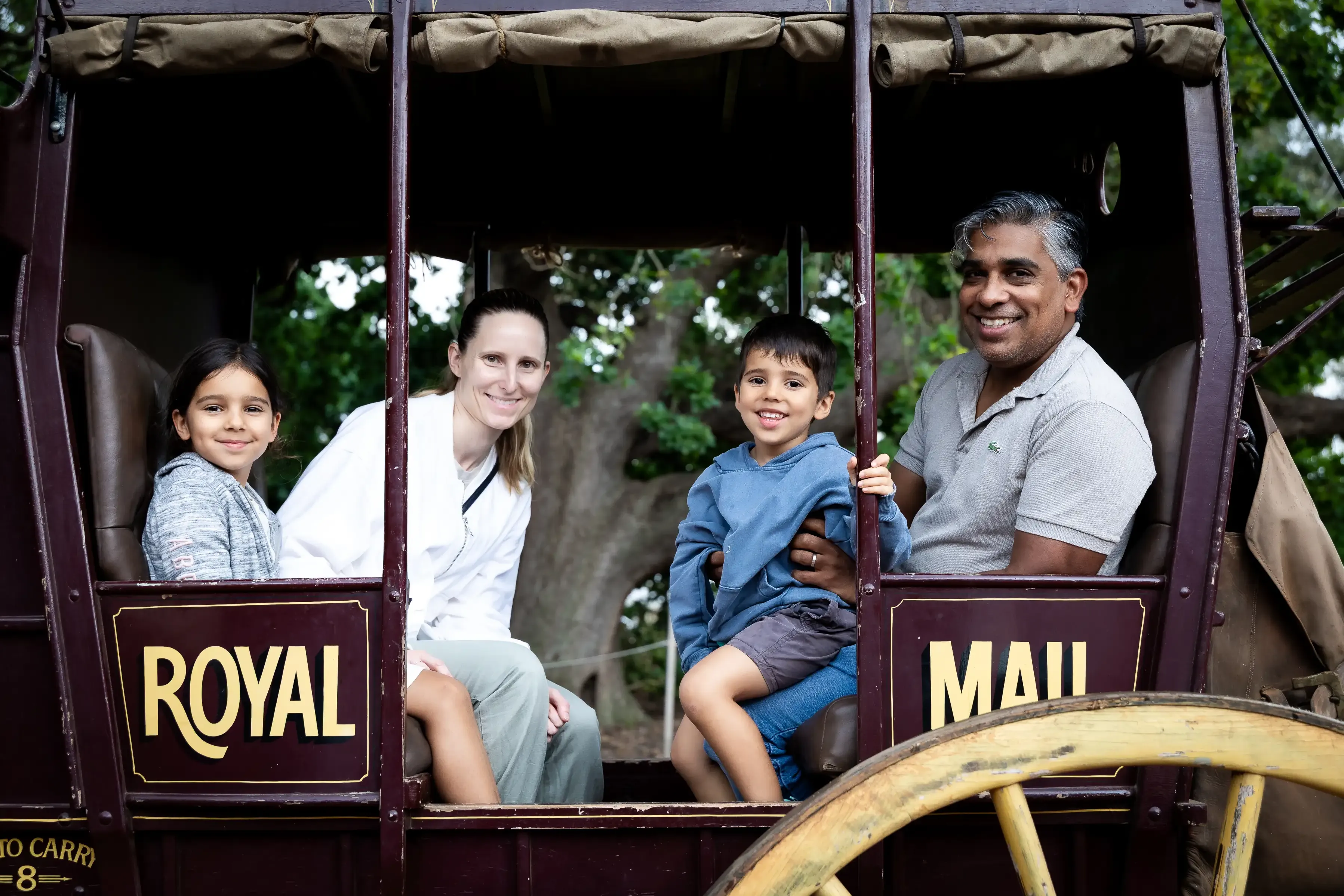 A family of four sits inside a historic horse-drawn mail coach, posing for a photo during a community event.