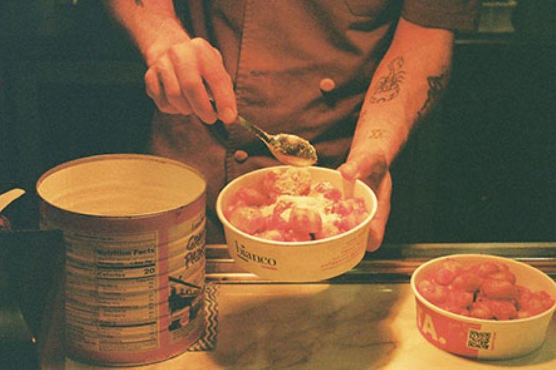 Person behind a gelato counter scoops gelato into a branded takeaway container.