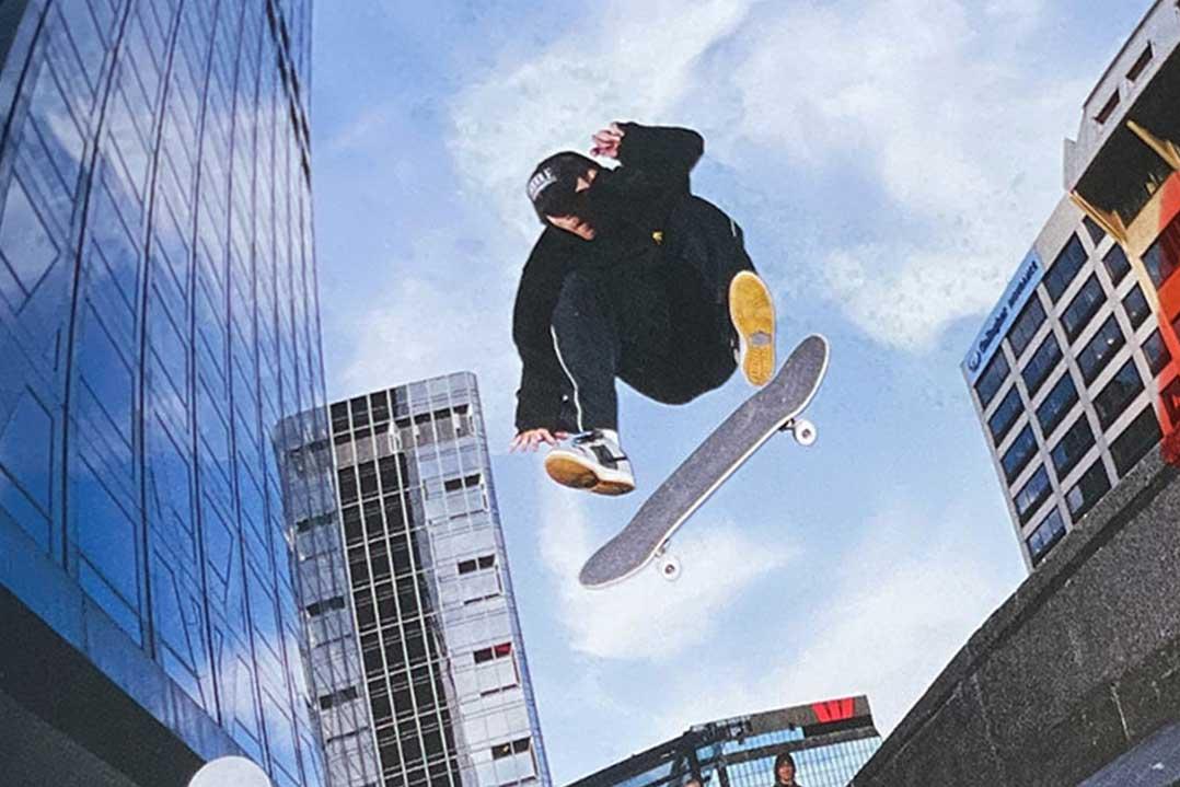 Skateboarder performs an airborne trick above a city plaza, framed by tall glass buildings and a bright blue sky; energetic urban scene.