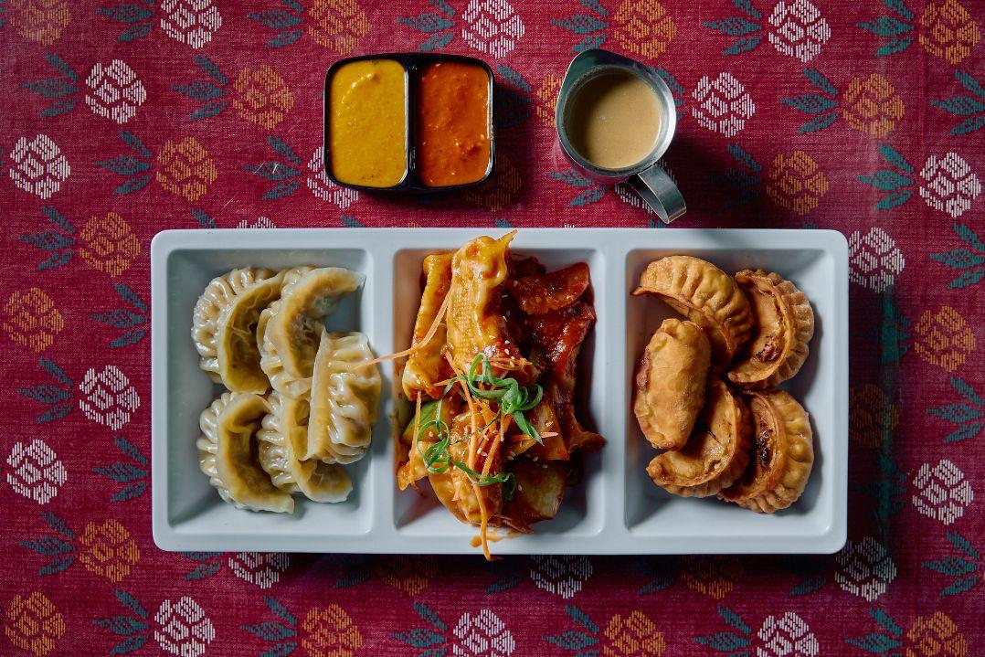 A divided serving platter featuring three varieties of dumplings on a patterned red tablecloth.