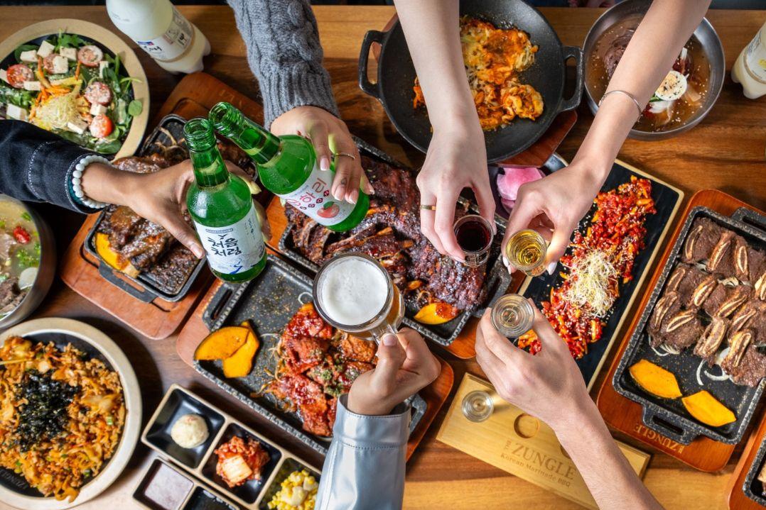 overview shot of food on a table with hands holding drinks to cheers