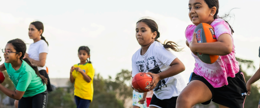 Girls running while holding a football in their arms and hands