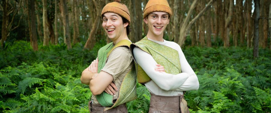 Two 2 smiling while standing in the bush and wearing leaves and yellow beanies to look like Snugglepot & Cuddlepie