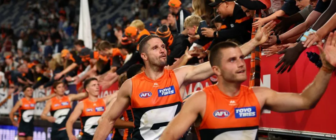 AFL players in orange and black uniforms high-five enthusiastic fans in matching colors, creating an energetic and celebratory atmosphere.