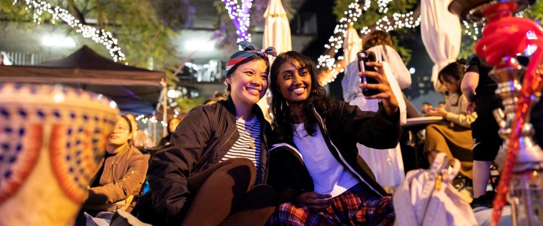 Two people sitting on a mat with fairy lights behind them