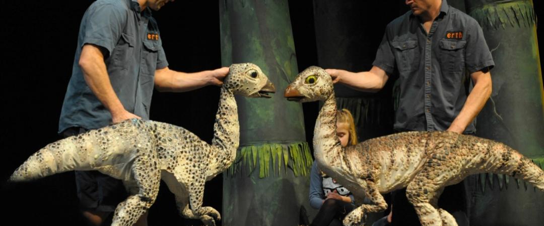 Two men in blue shirts holding dinosaur puppets