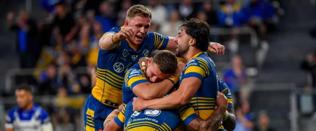 3 men in Parramatta Eels Jerseys of blue and yellow jumping on each other in celebration