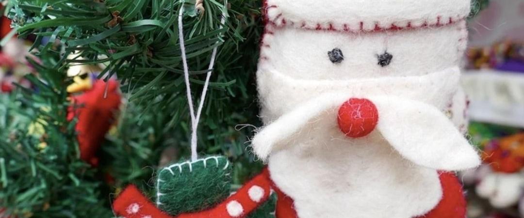 Festive handmade Santa decoration with a fuzzy white beard and red hat hanging on a Christmas tree, alongside colorful ornaments, conveying joy.