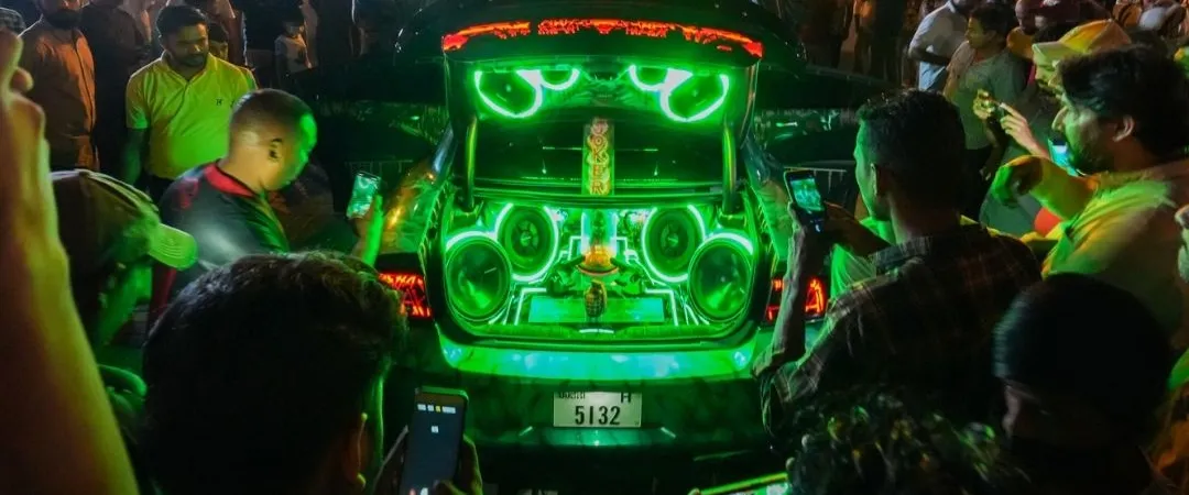 A man performs on a vibrant, green-lit stage in front of an engaged crowd at night. The energetic atmosphere suggests a lively event or festival.