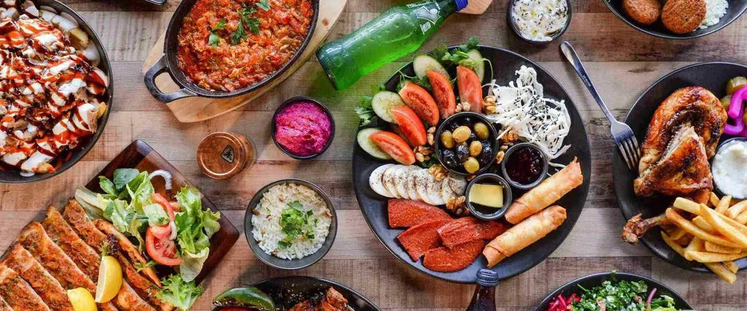 Overhead view of an abundant Mediterranean feast: grilled meats, hummus, salads, dips, bread, fries, seafood, and colorful vegetables.