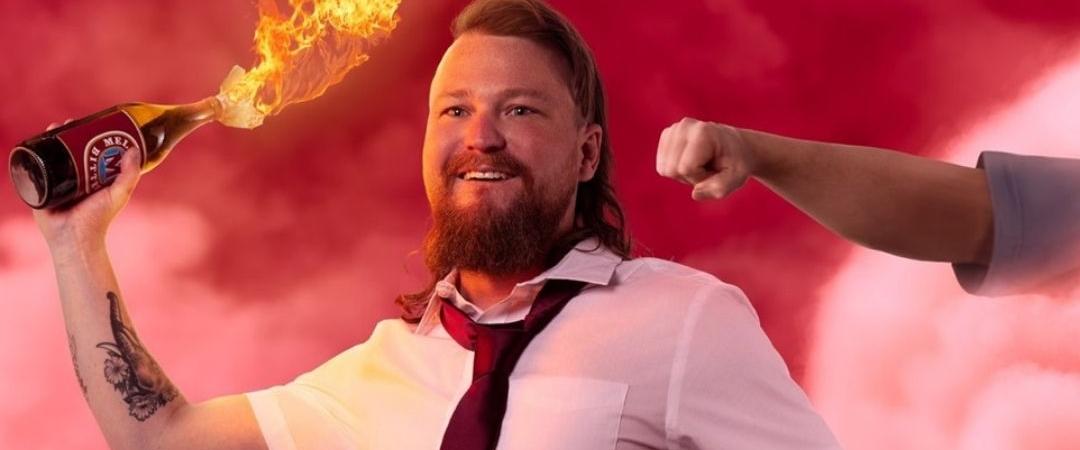 A bearded man in a white shirt and tie holds a flaming Molotov cocktail against a smoky red background while a fist approaches from the right. The scene is intense and dynamic.