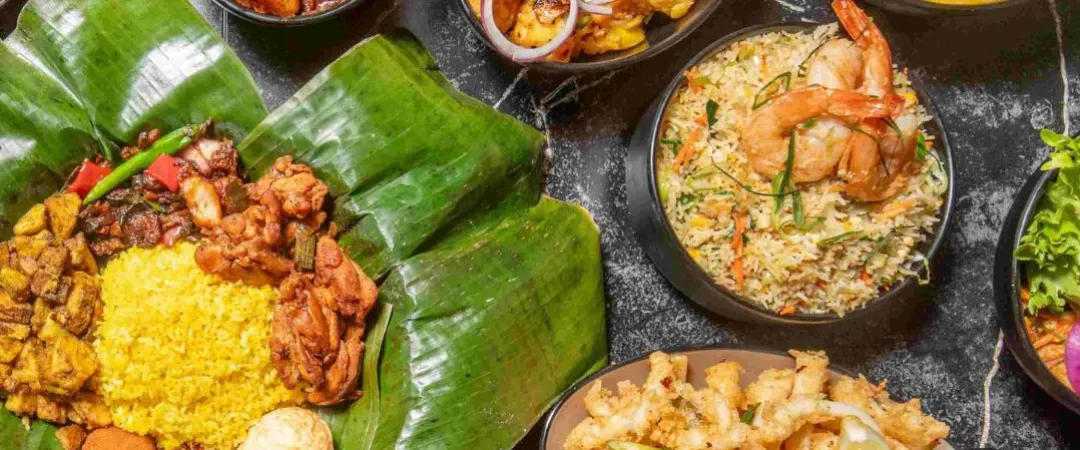 Overhead spread of vibrant Indian cuisine: banana-leaf thali, biryani with shrimp, curries, fried snacks, chutneys, and colorful garnishes.
