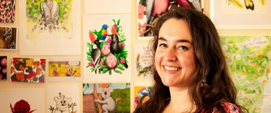 Person standing in front of a wall filled with colourful illustrations, comics and nature-inspired artworks, including birds, native plants, animals and landscapes.