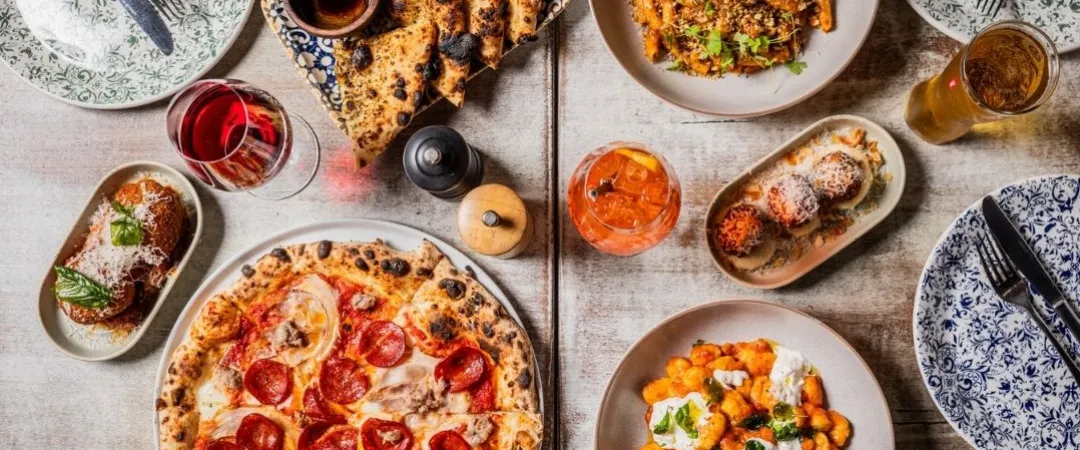 Table of pizza, pasta, arancini, meatballs and wine in glasses