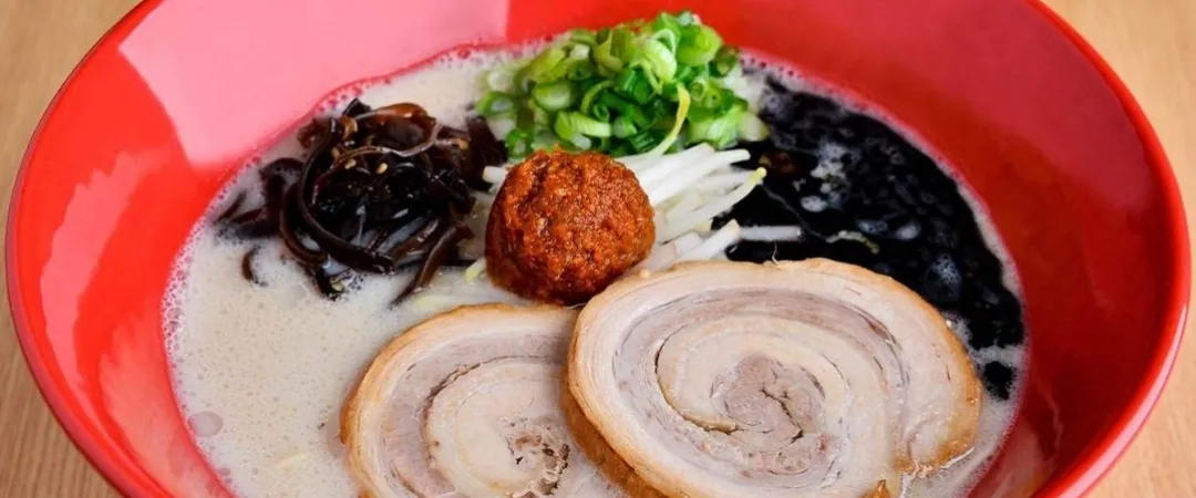 Large red bowl of ramen, so cloudy liquid with seafood and slim meat cuts