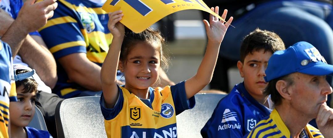 A young fan joyfully holds a large jersey in a stadium, surrounded by supporters in team colours, creating a lively and festive atmosphere.
