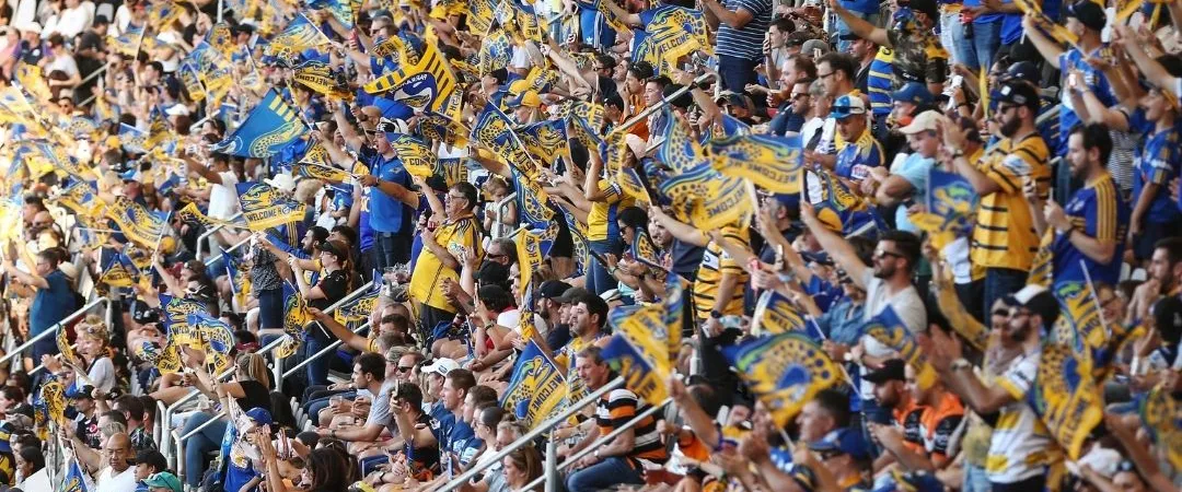 A vibrant crowd of sports fans fills a stadium, wearing blue and yellow, waving flags and banners, creating an energetic and festive atmosphere.