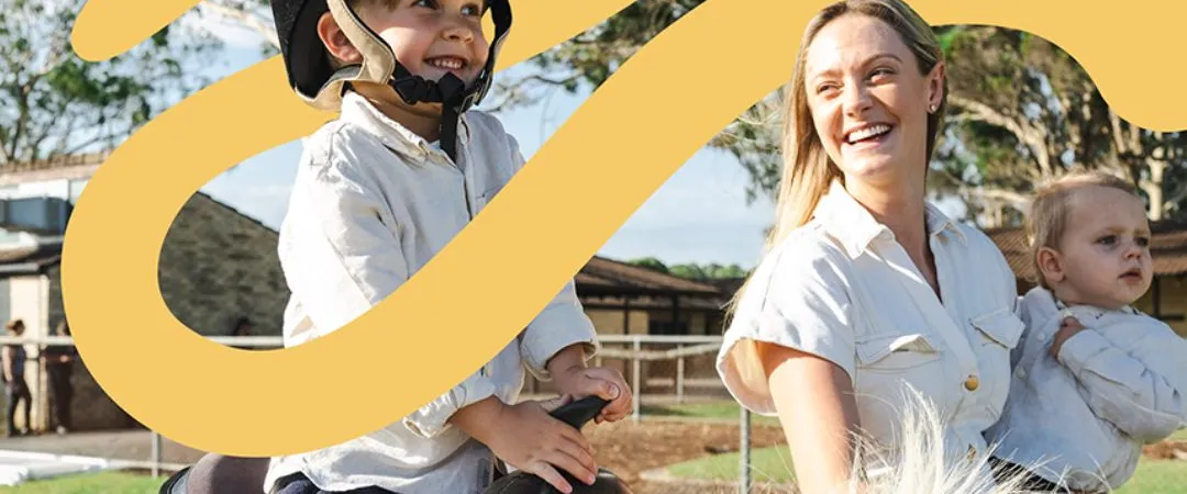 A child riding a horse and a lady holding a baby smiling and looking over at the child