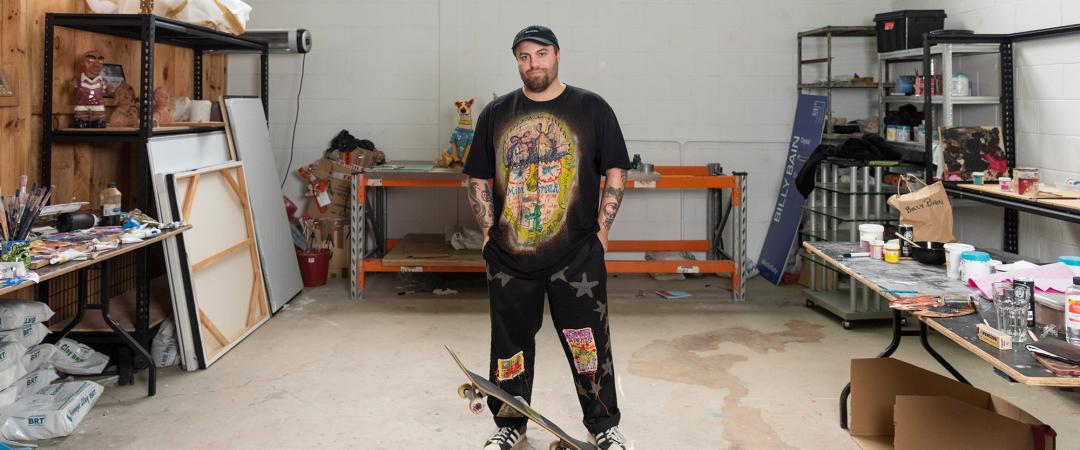 A man in all black standing inside an artist studio on top of a skateboard