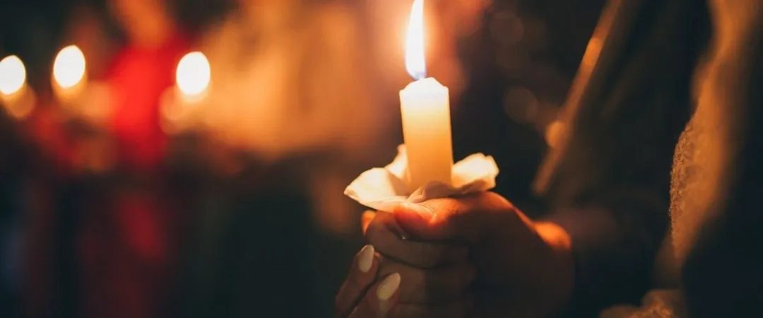 Hand holding lit up candle in a dark night time setting