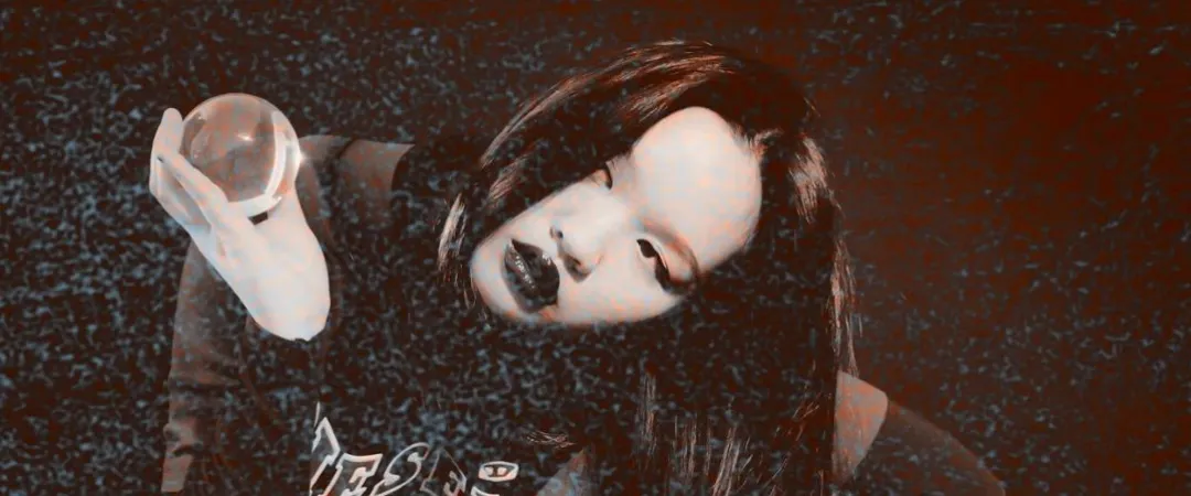 A person with long hair and dark lipstick gazes into the camera, holding a shiny orb. The photo has a textured, grainy overlay, creating a mysterious, artistic mood.