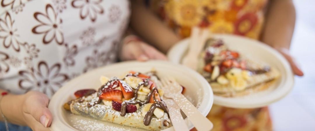 Hand holding a paper plate with a crepe covered in strawberries and nutella