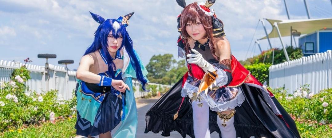 Two people in colorful fantasy costumes, one in blue with horns and the other in red with wings, strike dynamic poses on a sunny street, creating a playful and adventurous scene.