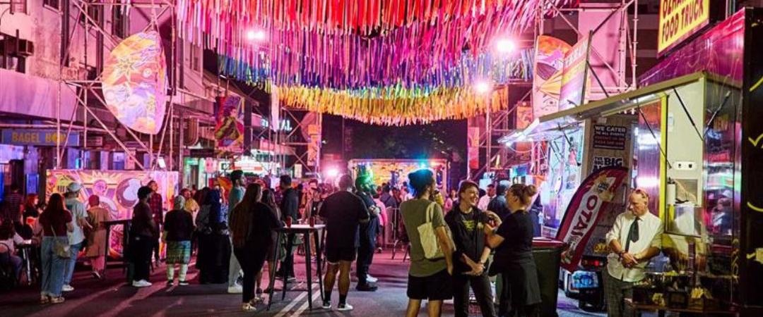 A bustling night market scene with colorful lanterns overhead, vibrant stalls lining the street, and a crowd of people enjoying the lively atmosphere.