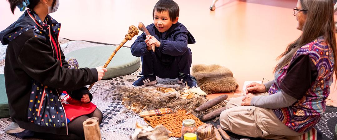 3 people sit in a circle looking at Aboriginal Artifacts
