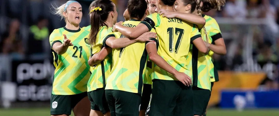 A group of female soccer players in yellow and green jerseys celebrate on the field, hugging each other joyfully, conveying a sense of teamwork and victory.