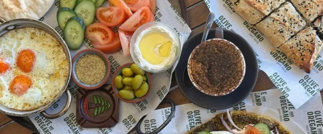 A colorful Mediterranean breakfast spread features fried eggs, cucumber and tomato slices, olives, yogurt, spices, flatbread, za’atar bread, and salad, invitingly arranged.