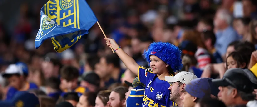 Young fan in blue waves a team flag at a crowded sports event. The audience is enthusiastic, creating an energetic and supportive atmosphere.