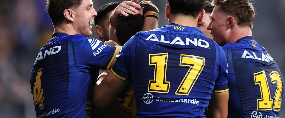 Rugby players in blue jerseys celebrate on the field, embracing and patting each other. The mood is joyful and triumphant, highlighting team spirit.