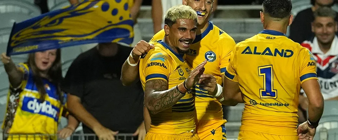 Rugby players in yellow jerseys celebrate a try, surrounded by cheering fans with team banners. The scene is joyful and energetic, capturing a moment of triumph.