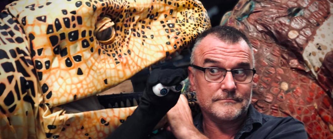 Man in black tshirt next to dinosaur puppet
