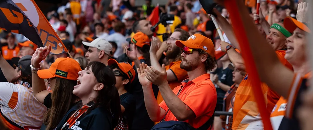 Enthusiastic crowd dressed in orange and black, cheering with flags and banners at a sports event, conveying excitement and camaraderie.