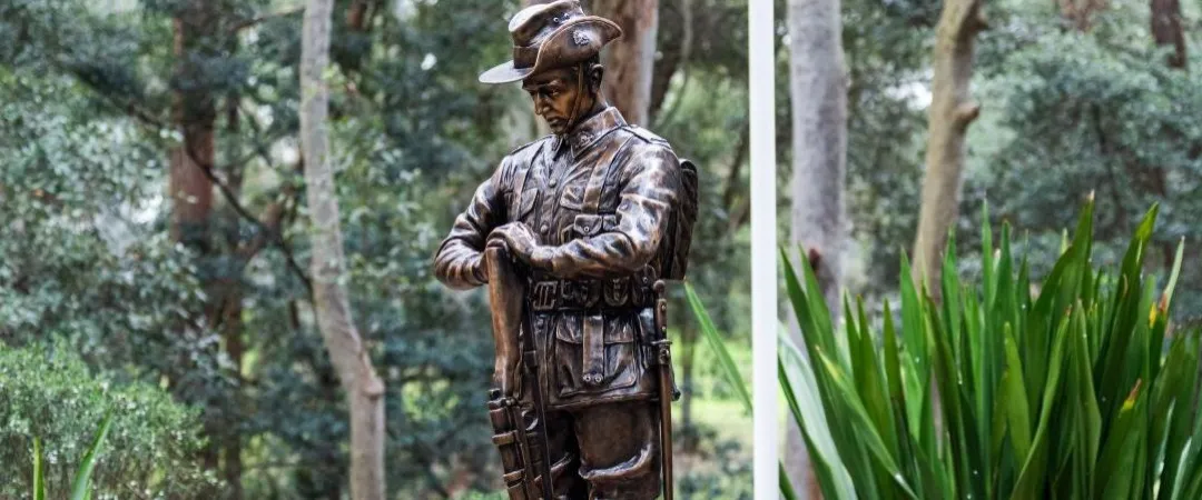 Bronze statue of a uniformed servicemember standing with head lowered and hands resting on a rifle.