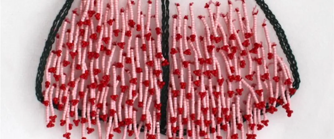 A beaded necklace with black braided string and pink beads, adorned with clusters of red beads resembling floral accents. The design is intricate and artistic.