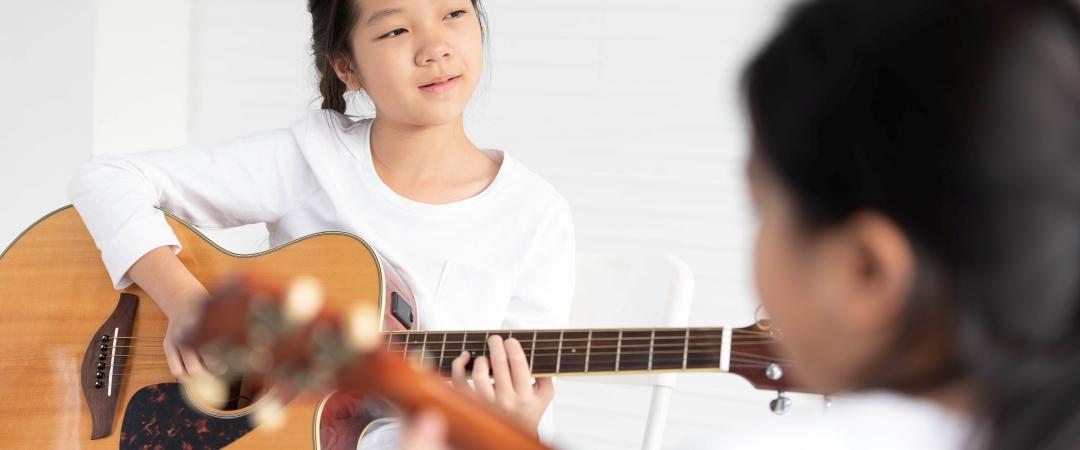 Girl holding guitar and wearing white long sleeve shirt