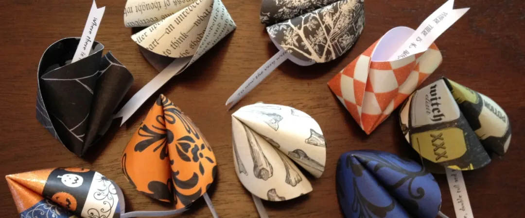Assorted handmade folded-paper ornaments in black, cream, orange, red, blue, and yellow rest on a wooden table, creating a whimsical, crafty display.