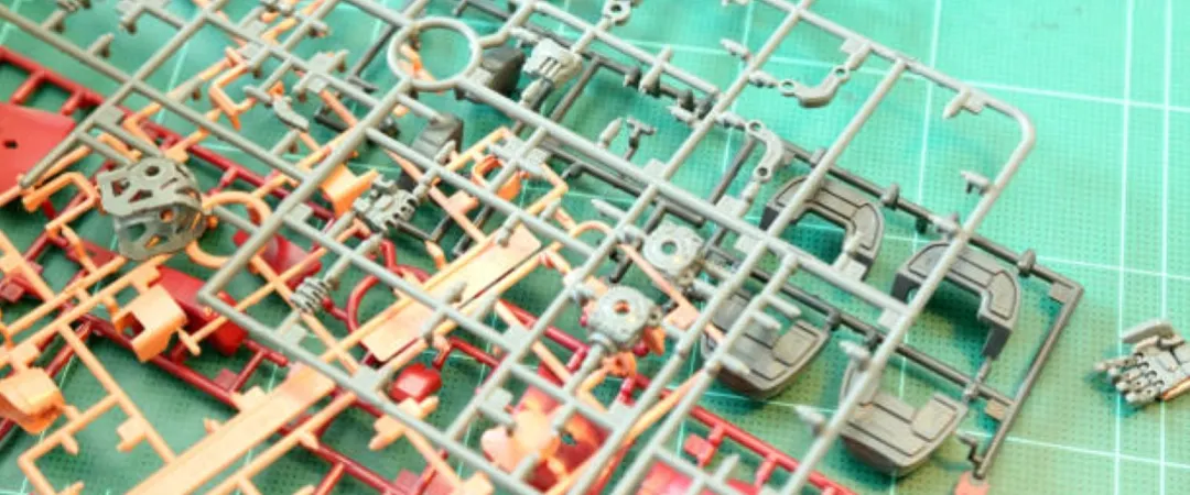 Close-up of plastic model kit sprues on a green cutting mat, with scattered small parts and a tool in the background, suggesting a model-building project.